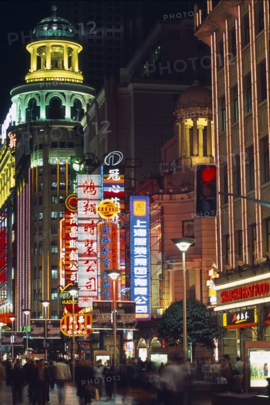 CHINA, Shanghai, Nanjing Road at night with illuminated neon signs and crowds of people in blurred movement below.