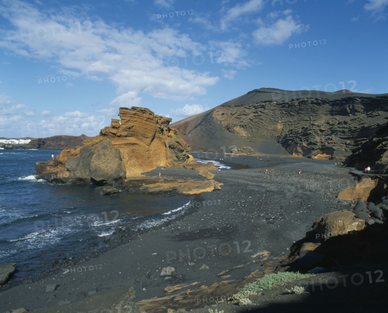 SPAIN, Canary Islands, Lanzarote, El Golfo.  Black volcanic sand beach and coastline with a few people sunbathing or walking along shore.