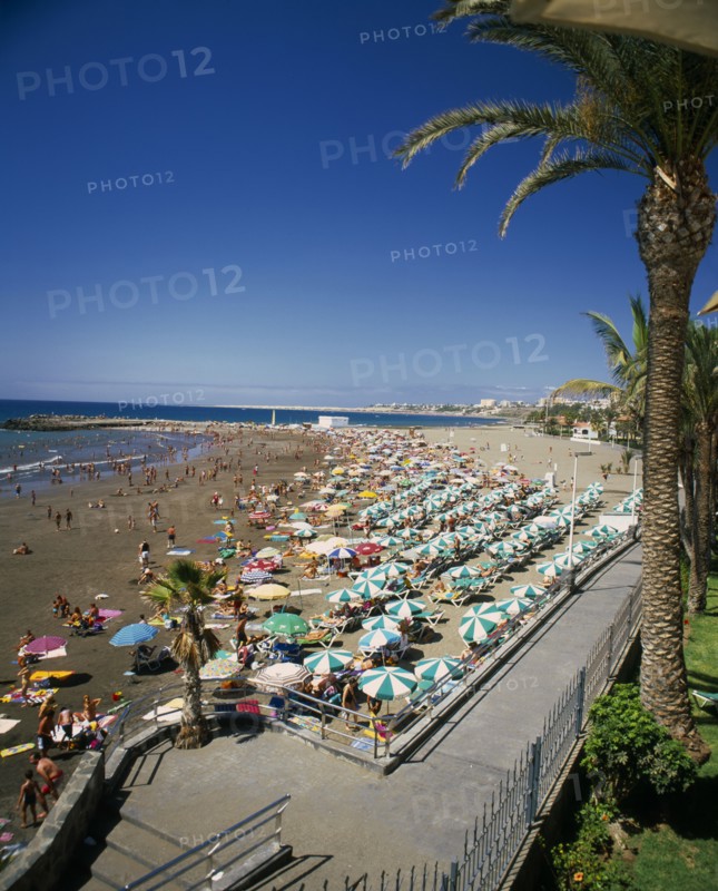 SPAIN, Canary Islands, Gran Canaria, San Augustin Playa de las Burras.  Sandy beach crowded with holidaymakers and lines of green and white sun loungers and sun umbrellas.