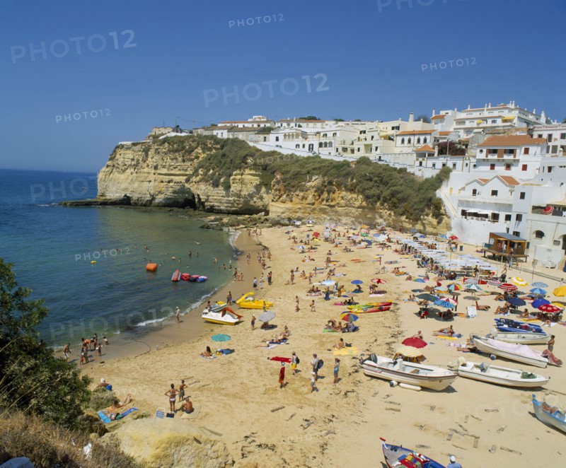 PORTUGAL, Algarve, Carvoeiro, White painted town on rocky headland overlooking busy beach.