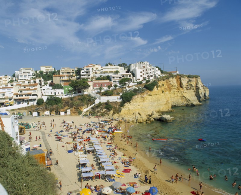 PORTUGAL, Algarve, Carvoeiro, White painted town on rocky headland overlooking busy beach.