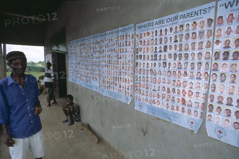 LIBERIA   , Margibi, Kakata, Man standing next to Red Cross tracing posters of Liberian children whose parents are missing