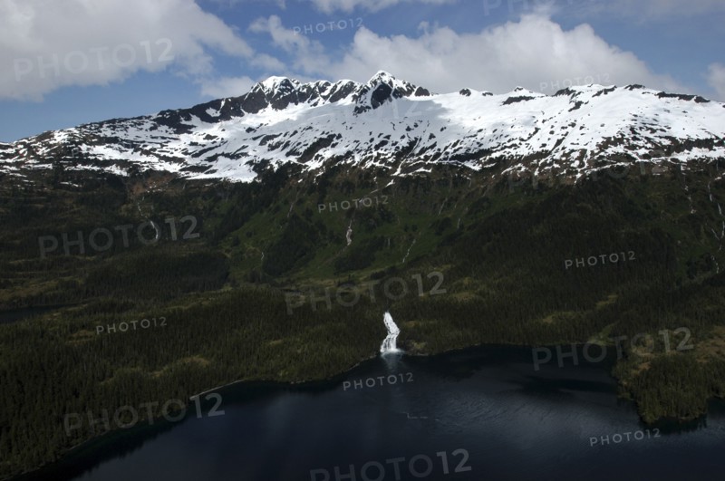 USA, Alaska, Prince William Sound, Aerial view over water and tree covered slopes leading toward snow capped mountain peaks