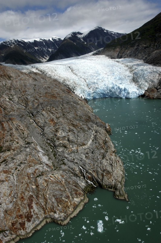 USA, Alaska, Tracy Arm Fjord, View over rocky edged waterway toward icy slope and mountain peaks beyond