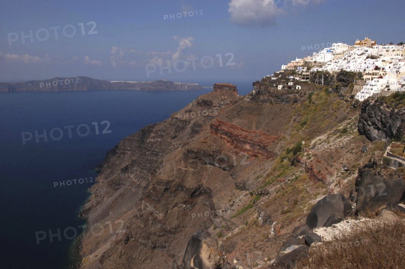 GREECE, Cyclades, Santorini, View along rugged coastal cliffs with the white architecture of the town nestled on the clifftop