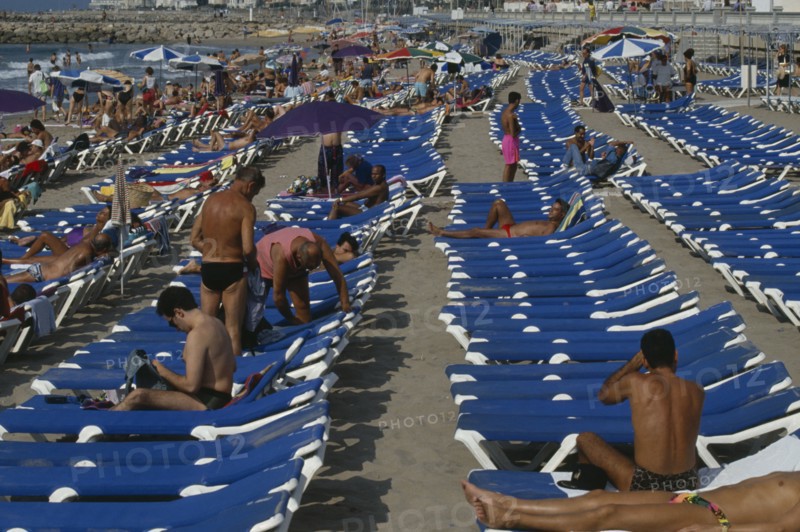 SPAIN, Catalonia, Sitges, Crowded beach with rows of blue sun loungers and sunbathers.
