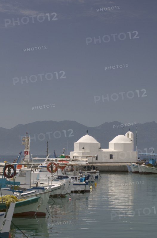 GREECE, Saronic Islands, Aegina, Fishing boats moored in Aegina Town next to a small white church with the mainland in the distance.