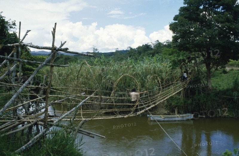 INDONESIA, Sulawesi, Napu Valley. Bamboo bridge over river with people crossing over.