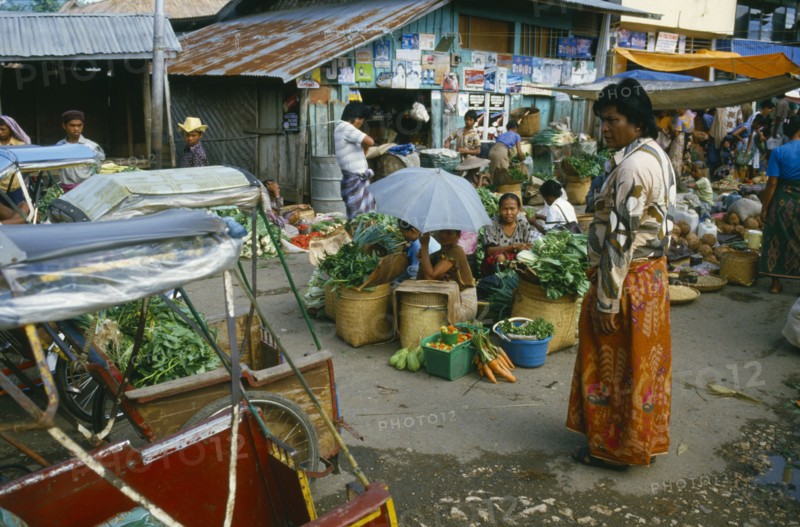 INDONESIA, Toraja, Market with sellers sitting around baskets of green vegetables with a market overseer looking on.