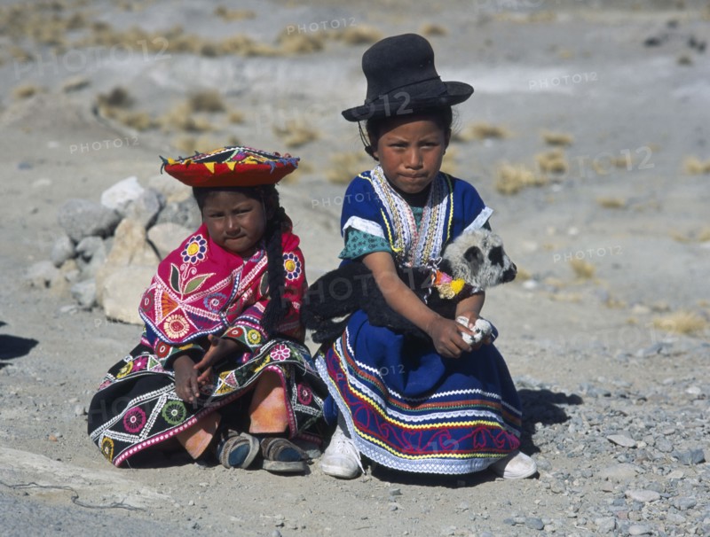 PERU, Near Arequipa, Two young children sitting on the ground with one holding a lamb