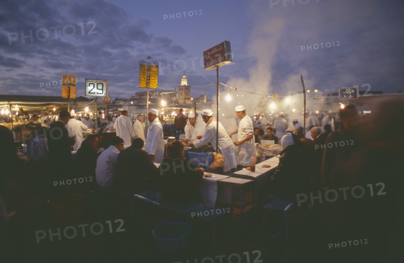 MOROCCO, Marrakesh, Djemaa el Fna. Food vendors serving up food to hungry customers seated around them at dusk