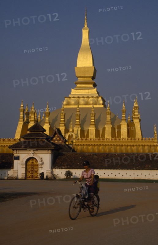 LAOS, Vientiane, Pha That Luang temple exterior with cyclist in foreground.