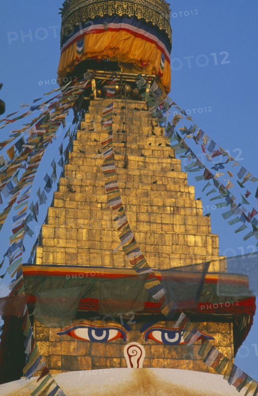 NEPAL, Kathmandu, Bodnath Stupa, Detail of spire of stupa with painted eyes and hung with prayer flags.