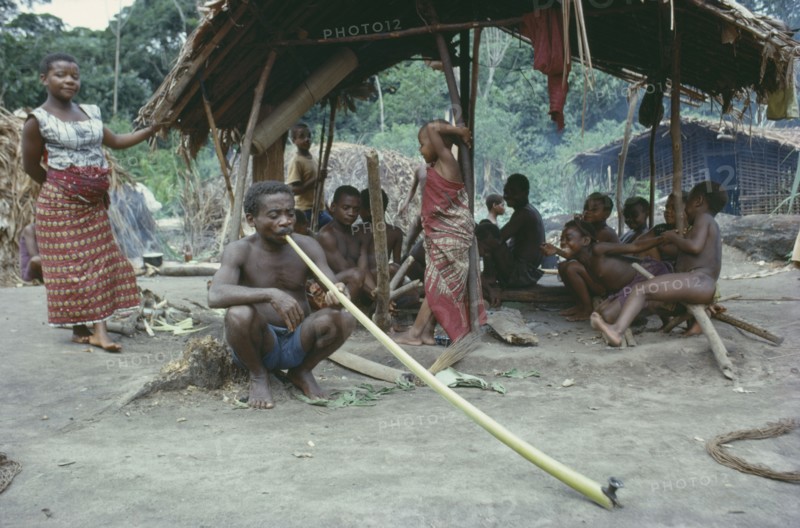 CONGO, Tribal Peoples, Pygmies in forest near Ituri.  Man in foreground smoking dried local leaves in long bamboo pipe.