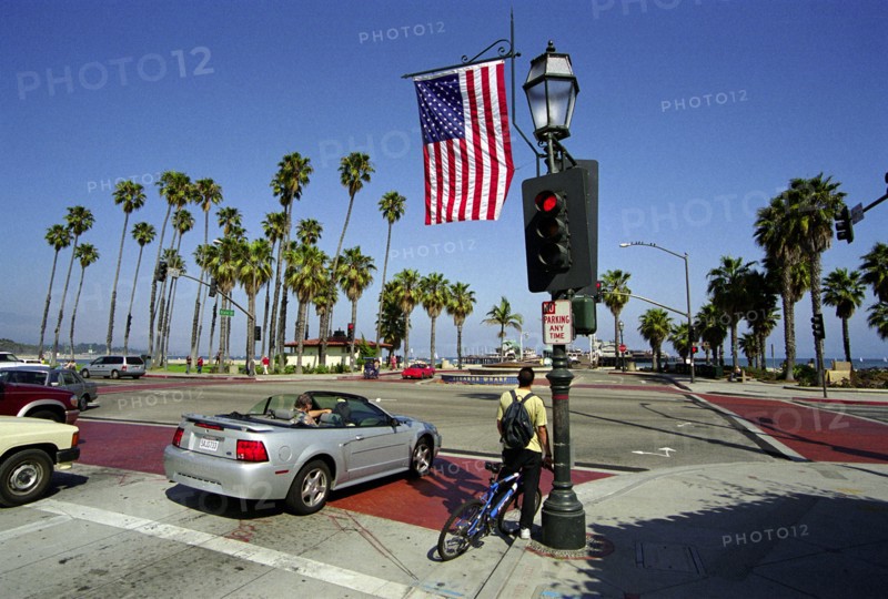 USA, California, Santa Barbara, Traffic lights with flag at the junction of State Street and Cabrillo Blvd. looking out toward Stearns Wharf and West Beach