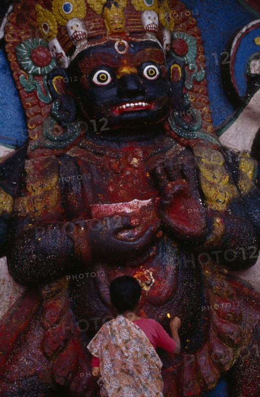 NEPAL,  , Kathmandu, Woman making offerings at the Kala Bhairab or black Shiva in Durbar Square representing the fearsome Tantric form of Shiva in Nepal.
