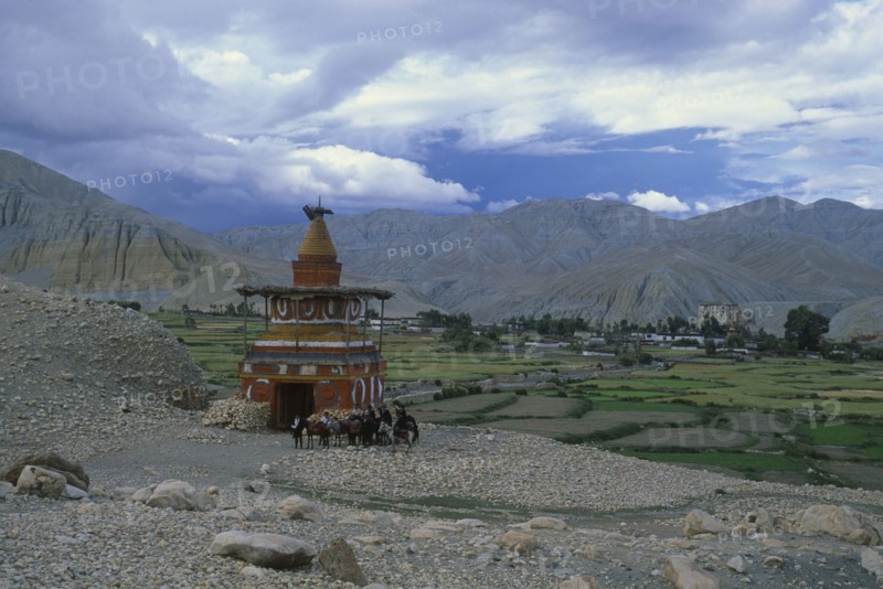 NEPAL, Mustang, Tsarang, Group of riders on ponies beside stupa marking the entrance to Tsarang.