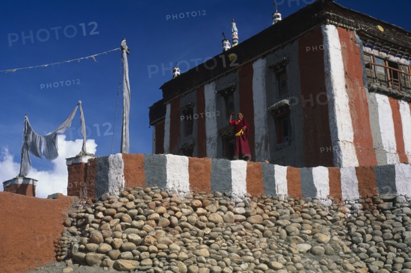 NEPAL, Mustang, Tsarang, Head monk looking out from terrace of temple painted with coloured stripes.