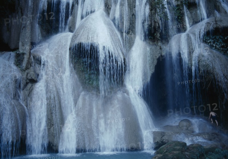 LAOS, Luang Prabang Prov., Kuang Si Falls, Close view of waterfall with man climbing rocks at side.