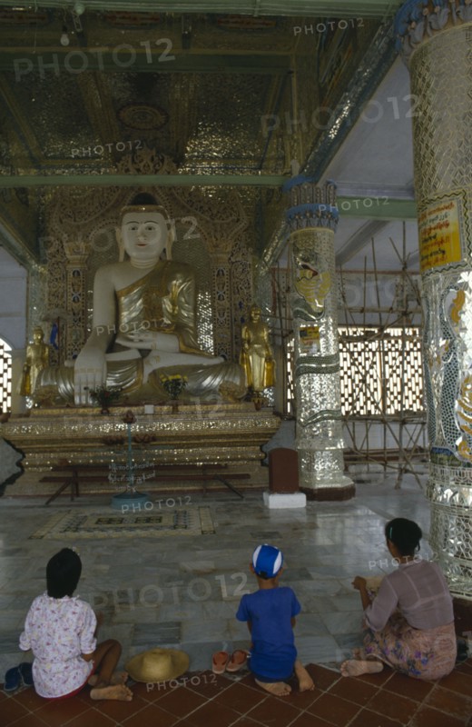 MYANMAR, Sagaing, Woman and children kneeling in front of giant seated Buddhist figure.
