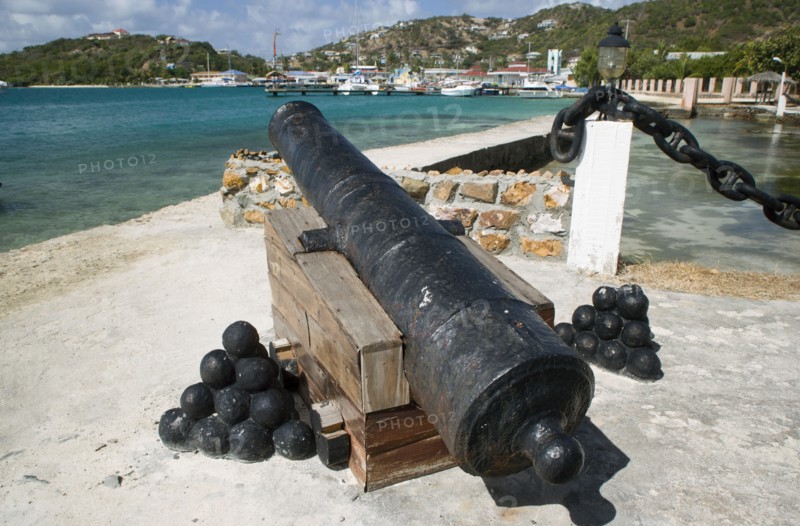 WEST INDIES, St Vincent & The Grenadines, Union Island, Ancient canon on the harbourside at Clifton with the town and mooring behind