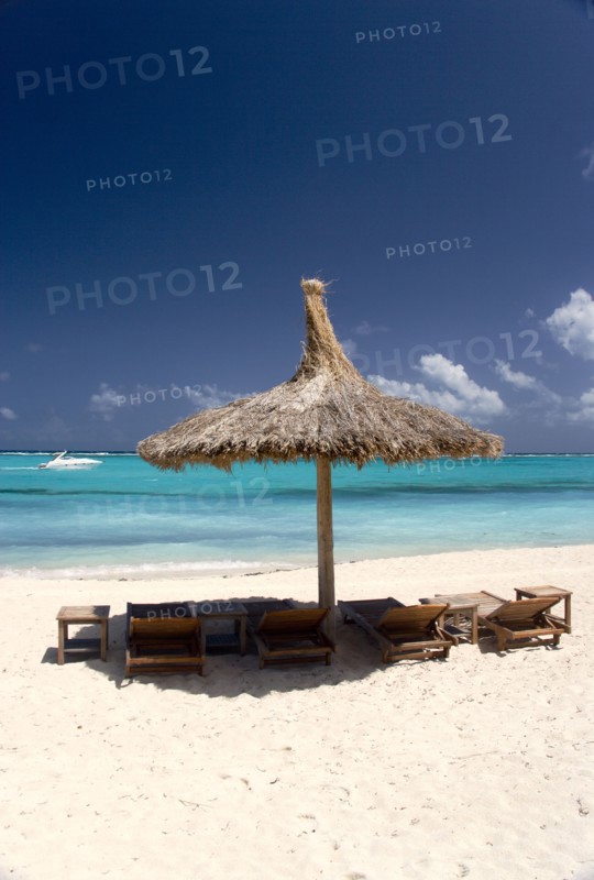 WEST INDIES, St Vincent & The Grenadines, Canouan, Palapa thatched shelter and sunbeds on Godahl Beach at Raffles Resort with speedboat passing along the bay