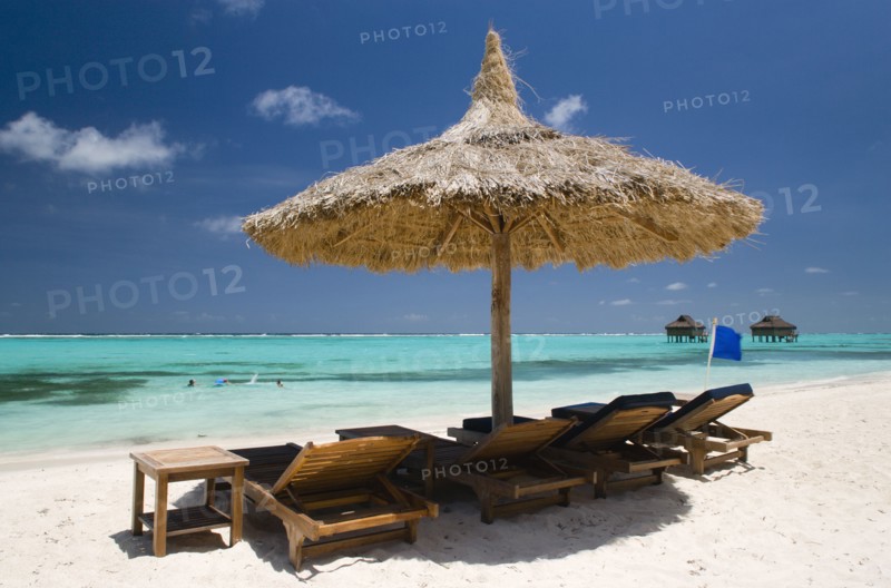 WEST INDIES, St Vincent & The Grenadines, Canouan, Palapa thatched shelter and sunbeds on Godahl Beach at Raffles Resort with offshore treatment rooms of the Amrita Spa beyond