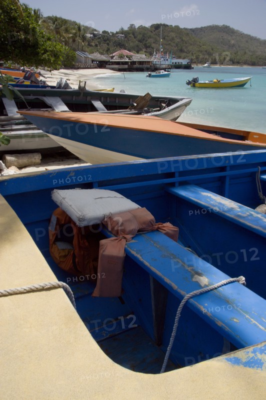 WEST INDIES, St Vincent & The Grenadines, Mustique, Fishing boats on the beach in Britannia Bay with Basils Bar beyond