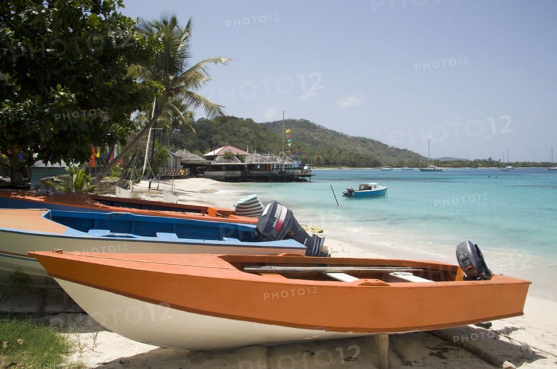 WEST INDIES, St Vincent & The Grenadines, Mustique, Fishing boats on beach in Britannia Bay with Basils Bar beyond