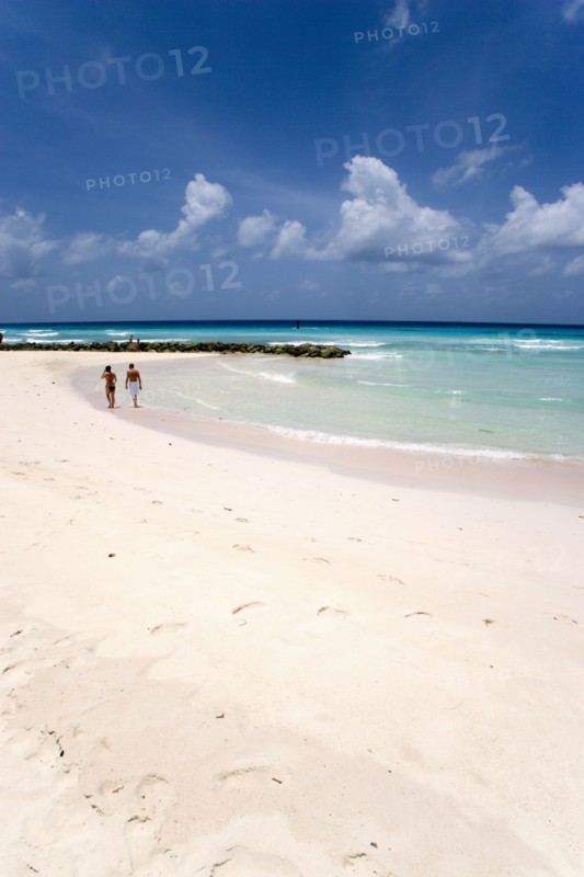WEST INDIES, Barbados, Christ Church, Couple walking towards sea defences on Rockley Beach also known as Accra Beach after the hotel there