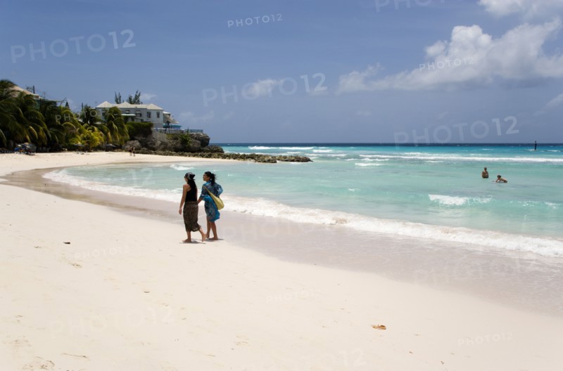 WEST INDIES, Barbados, Christ Church, Two women walking on the sand past a couple in the sea at Rockley Beach also known as Accra Beach after the hotel there