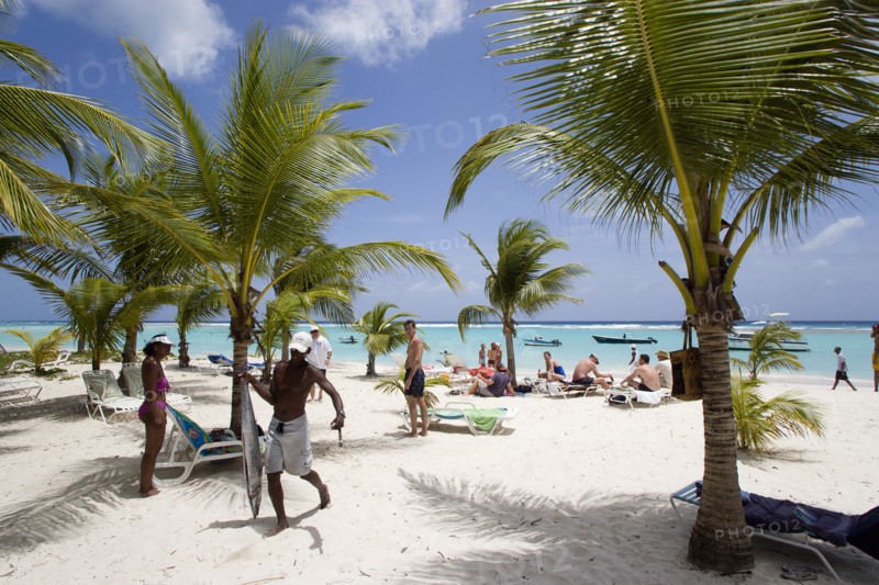 WEST INDIES, Barbados, Christ Church, Fisherman carrying gutted King Fish past tourists and coconut trees on Worthing Beach
