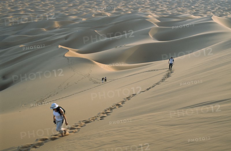 MOROCCO, Sahara, Merzouga, Tourists walking through desert landscape leaving trails of footprints across the dunes.