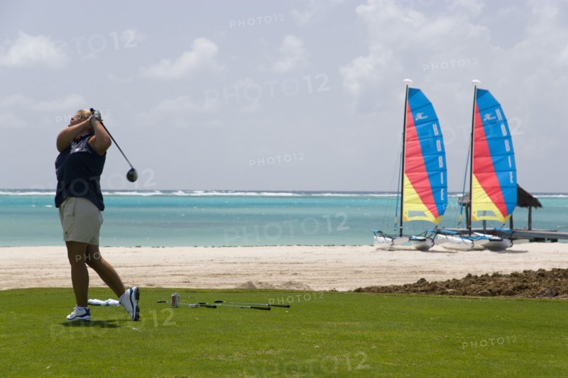 WEST INDIES, St Vincent & The Grenadines, Canouan, Lady golfer teeing off on the Raffles hotel practice range with beach and hobbie cats behind