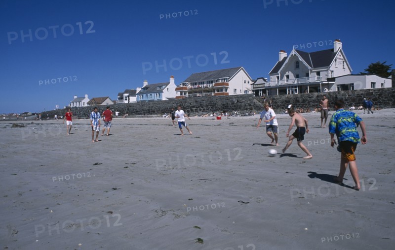 UNITED KINGDOM, Channel Islands, Guernsey, Castel. Cobo Bay. Young men playing football on sandy beach