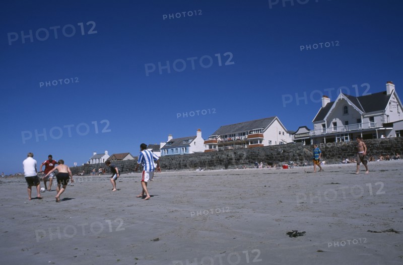 UNITED KINGDOM, Channel Islands, Guernsey, Castel. Cobo Bay. Young men playing football on sandy beach