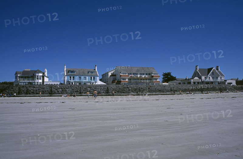 UNITED KINGDOM, Channel Islands, Guernsey, Castel. Cobo Bay. View across sandy beach with sunbathers and people playing football towards hotels and restaurants