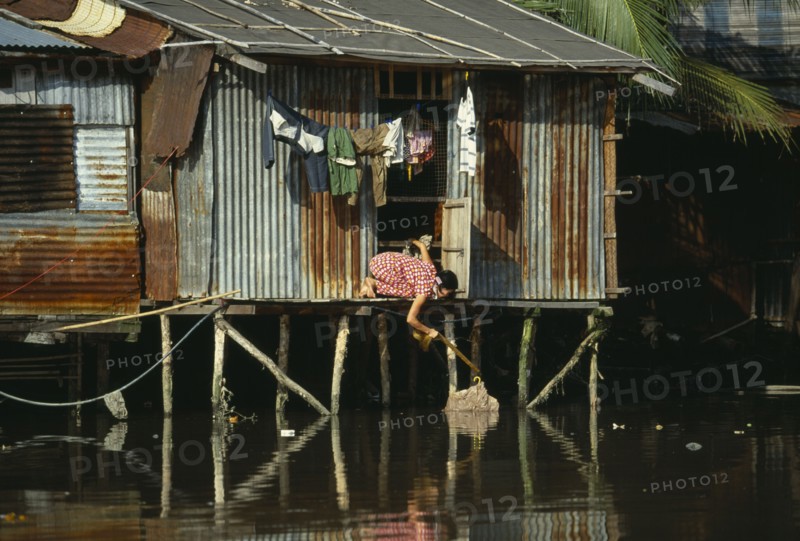 VIETNAM, South, Ho Chi Minh City, "Woman retrieving her washing from the Rach Thi Nghe backwater of the Saigon River, kneeling from doorway of tin hut built on wooden stilts."