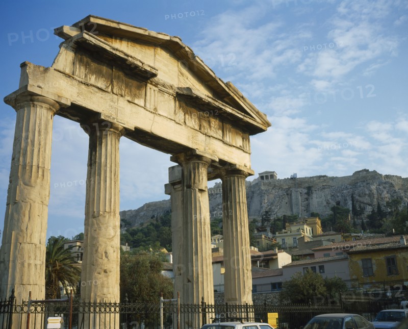 GREECE, Central, Athens, Plaka - Ancient Agora and Acropolis on top. Old ruined columns behind a fence with houses and a hill in the background.