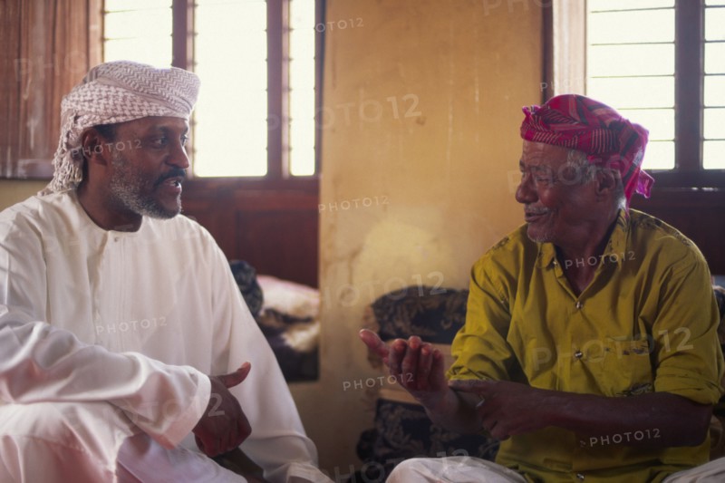 OMAN, Sur, "Discussioin between two Omanis, including traditional fisherman on the right hand side."