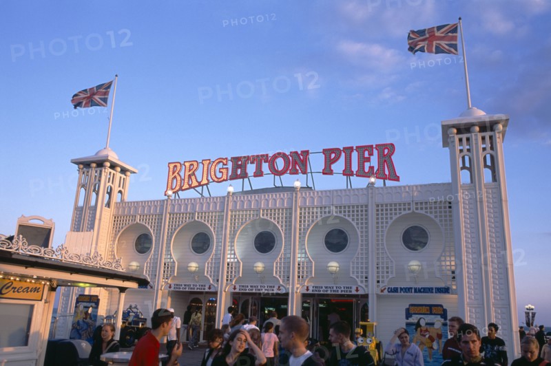 ENGLAND, East Sussex, Brighton, Brighton Pier with groups of people in the foreground.