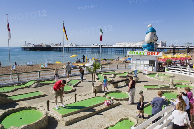 ENGLAND, East Sussex, Brighton, Tourist family playing crazy golf on the seafront with Brighton Pier beyond