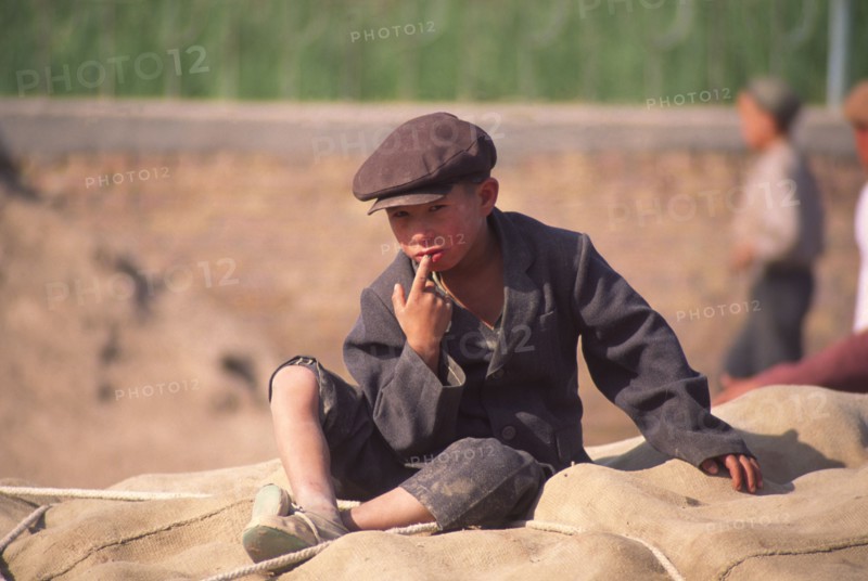 CHINA, Xinjiang Province, Kashgar,  Tajik boy sat on sacks