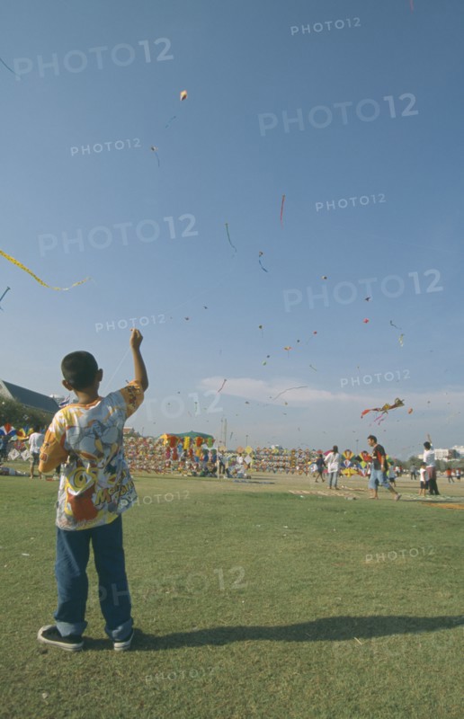THAILAND, Bangkok, "Kite festival at Sanam Luang, February. Boy flying one in foreground, many others in sky."