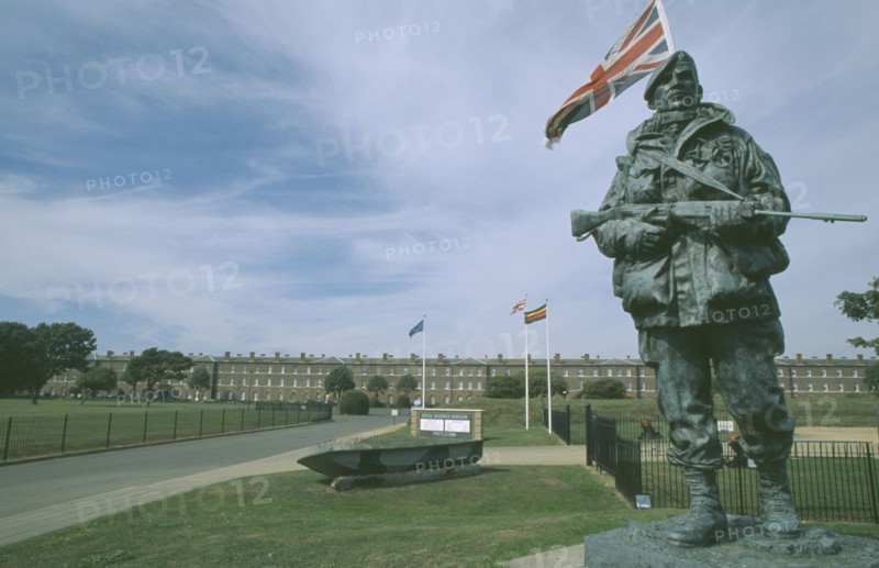 ENGLAND, Hampshire, Portsmouth, Royal Marines Museum. Large statue of a Royal Marine holding gun on display in front of building and Union Jack flag flying behind.