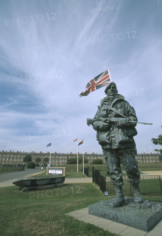 ENGLAND, Hampshire, Portsmouth, Royal Marines Museum. Large statue of a Royal Marine holding gun on display in front of building and Union Jack flag flying behind.