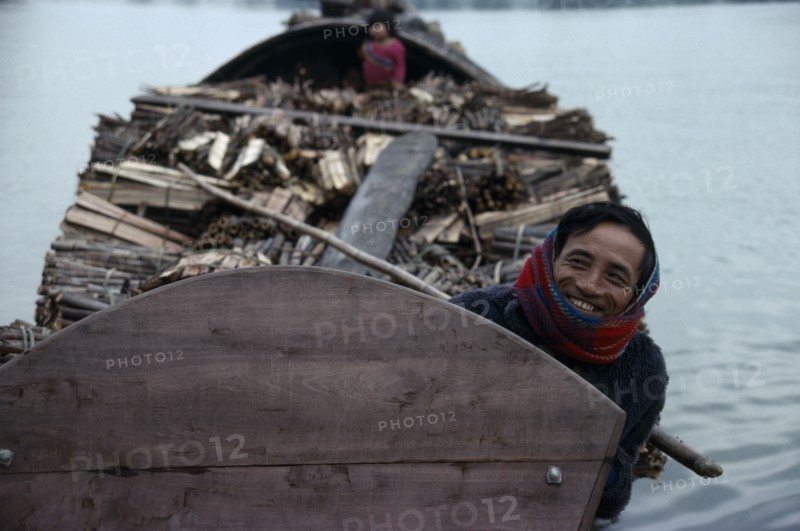VIETNAM, Central, Hue, Smiling boatman on barge laden with timber.