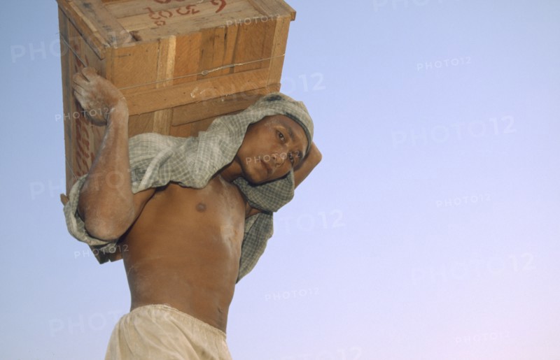 MYANMAR, Mandalay Dock, "Man carrying a crate above his head, wearing head scarf. Banks of the Irrawaddy"