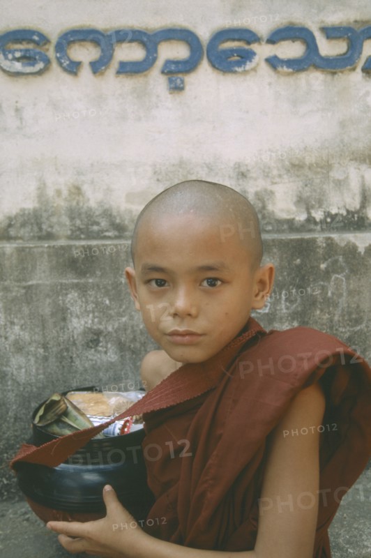 MYANMAR, Kawthoung, Young novice monk with bowl full of Alms offerings.