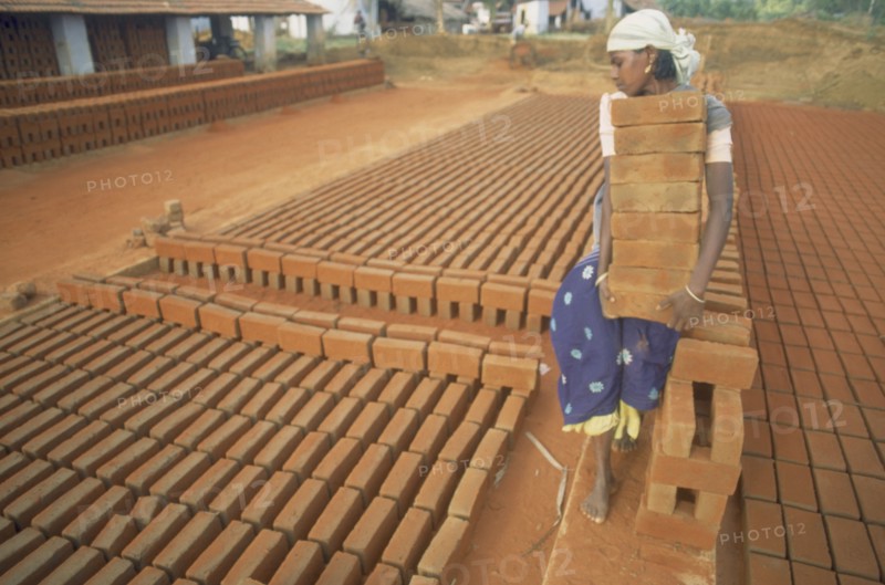 INDIA, Tamil Nadu, Barefooted young woman carrying large stack of bricks at brick works.